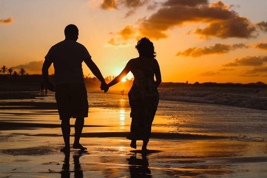 Pareja cogida de la mano caminando por la playa al atardecer